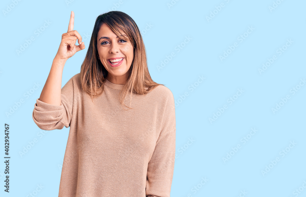 Young beautiful woman wearing casual sweater pointing finger up with successful idea. exited and happy. number one. Young beautiful woman wearing casual sweater pointing finger up with successful idea. exited and happy. number one.