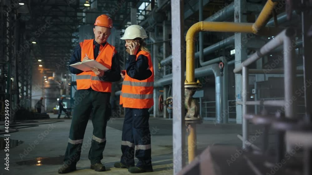 Recording information on clipboard. Shot of two cheerful workers in hardhat and protective uniform working at hardware factory manufacturing production plant positivity success teamwork collaboration Recording information on clipboard. Shot of two cheerful workers in hardhat and protective uniform working at hardware factory manufacturing production plant positivity success teamwork collaboration