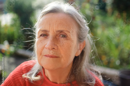 Close up face of happy senior woman with grey hair looking at camera while spending time outdoors during sunny day