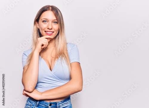 Young blonde woman wearing casual clothes smiling looking confident at the camera with crossed arms and hand on chin. thinking positive.