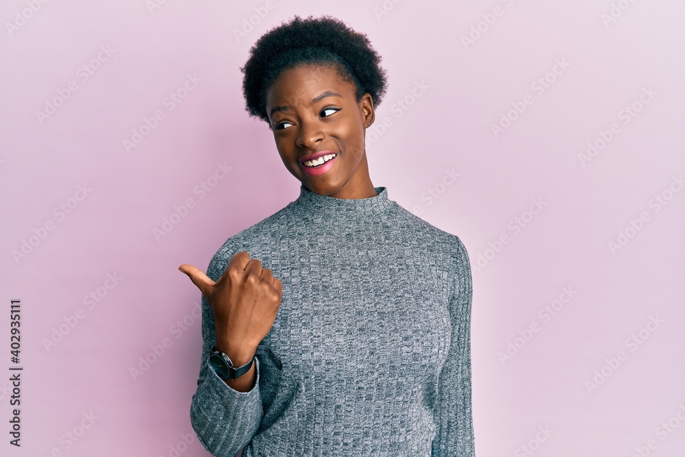 Young african american girl wearing casual clothes smiling with happy face looking and pointing to the side with thumb up.