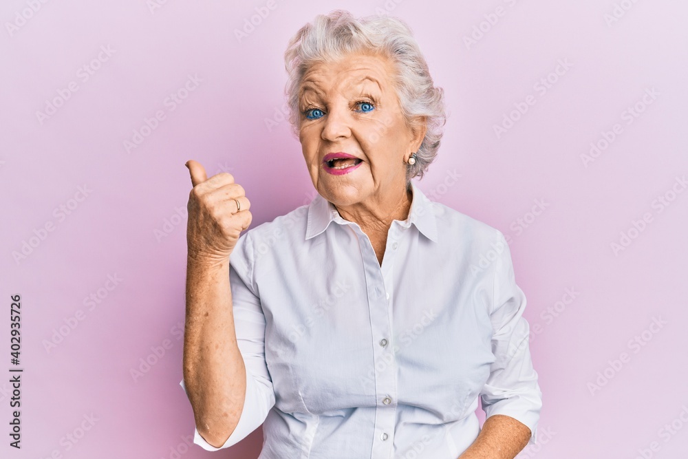 Senior grey-haired woman wearing casual clothes pointing thumb up to the side smiling happy with open mouth Senior grey-haired woman wearing casual clothes pointing thumb up to the side smiling happy with open mouth