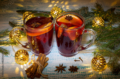 Hot mulled wine with orange  anise and cinnamon on the background of Christmas tree branches and garland. Warming Christmas drink. Festive mood.