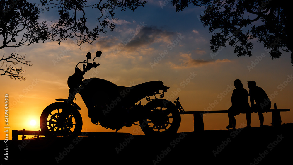 silhouette big bike motorcycle with couple sitting together on mountain peak  at sunset