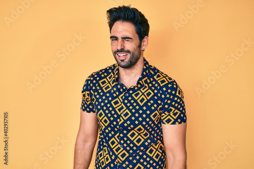 Handsome hispanic man with beard wearing 80s disco style shirt winking looking at the camera with sexy expression  cheerful and happy face.