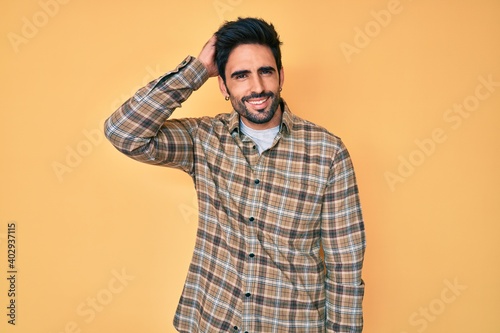Handsome hispanic man with beard wearing casual clothes confuse and wonder about question. uncertain with doubt, thinking with hand on head. pensive concept.