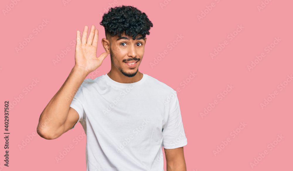 Young arab man wearing casual white t shirt waiving saying hello happy and smiling, friendly welcome gesture Young arab man wearing casual white t shirt waiving saying hello happy and smiling, friendly welcome gesture