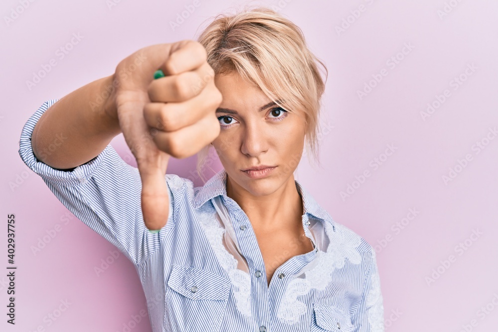 Young blonde girl wearing casual clothes looking unhappy and angry showing rejection and negative with thumbs down gesture. bad expression.