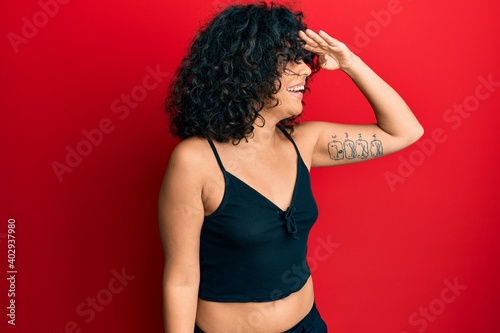 Young hispanic woman wearing casual style with sleeveless shirt very happy and smiling looking far away with hand over head. searching concept.