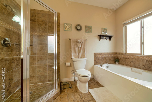 Shower stall toilet and built in bathtub inside bathroom with warm toned tiles