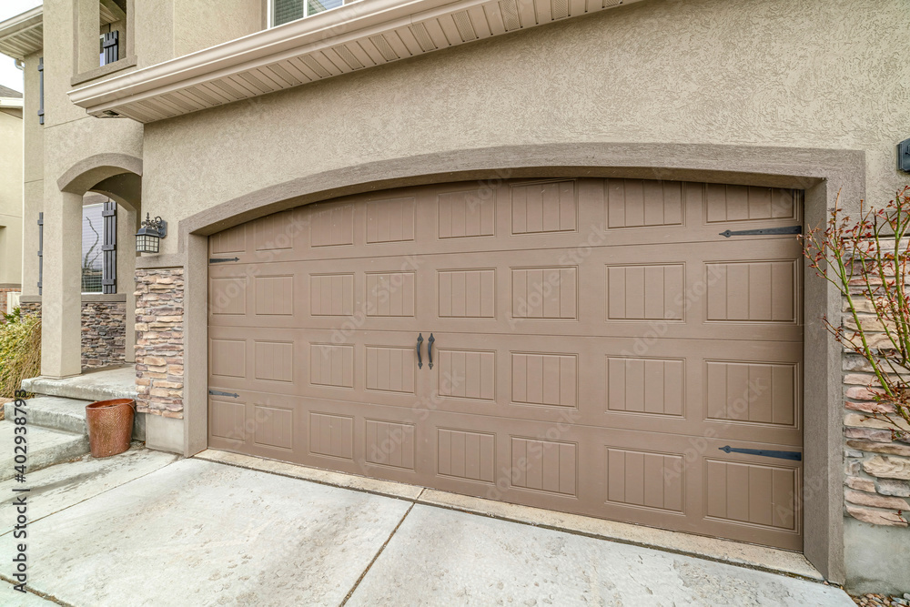 Attached garage of house with gray hinged paenelled doors and paved driveway