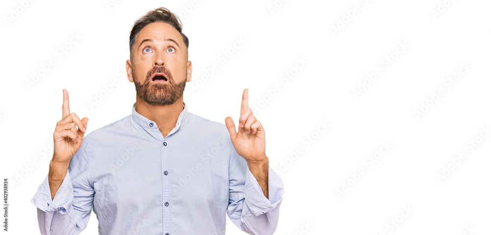 Handsome middle age man wearing business shirt amazed and surprised looking up and pointing with fingers and raised arms. Handsome middle age man wearing business shirt amazed and surprised looking up and pointing with fingers and raised arms.