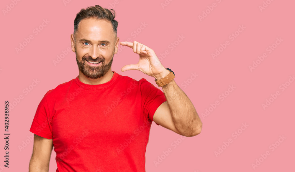 Handsome middle age man wearing casual red tshirt smiling and confident gesturing with hand doing small size sign with fingers looking and the camera. measure concept. Handsome middle age man wearing casual red tshirt smiling and confident gesturing with hand doing small size sign with fingers looking and the camera. measure concept.