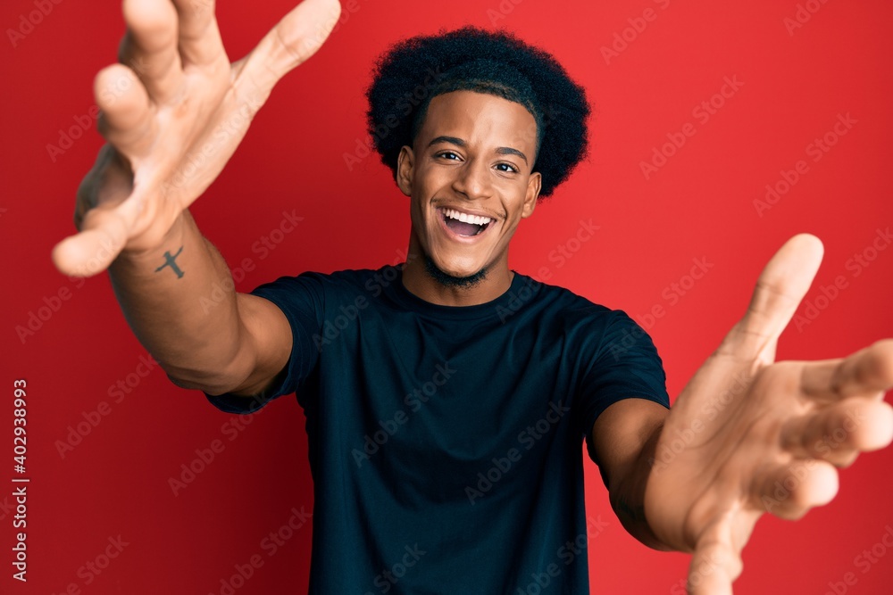 African american man with afro hair wearing casual clothes looking at the camera smiling with open arms for hug. cheerful expression embracing happiness. African american man with afro hair wearing casual clothes looking at the camera smiling with open arms for hug. cheerful expression embracing happiness.