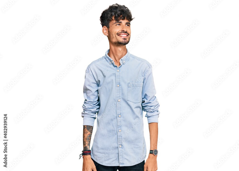 Fototapeta premium Young hispanic man wearing casual clothes looking away to side with smile on face, natural expression. laughing confident.
