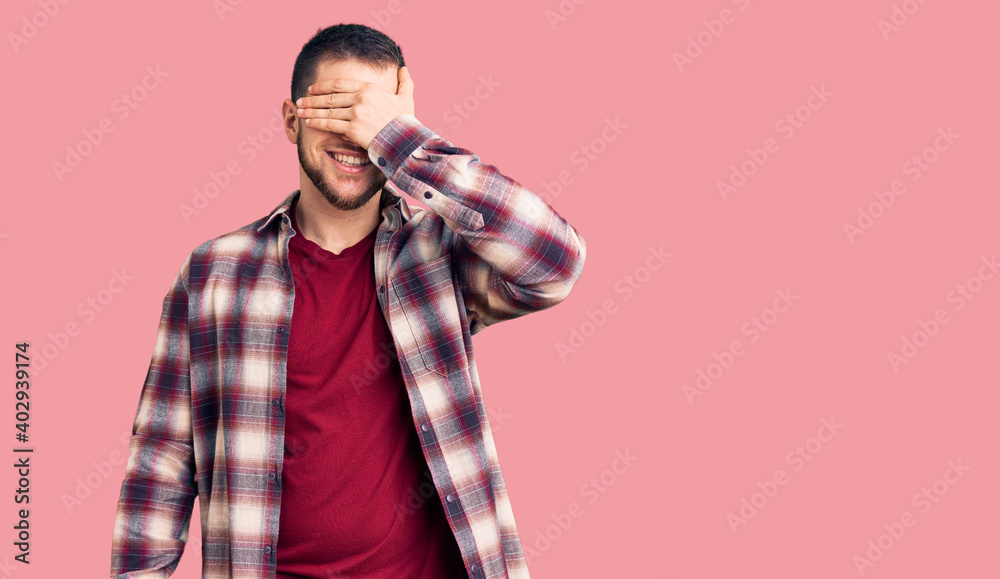 Young handsome man wearing casual shirt smiling and laughing with hand on face covering eyes for surprise. blind concept.