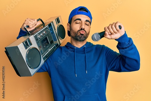 Young hispanic man holding boombox, listening to music singing with microphone looking at the camera blowing a kiss being lovely and sexy. love expression.