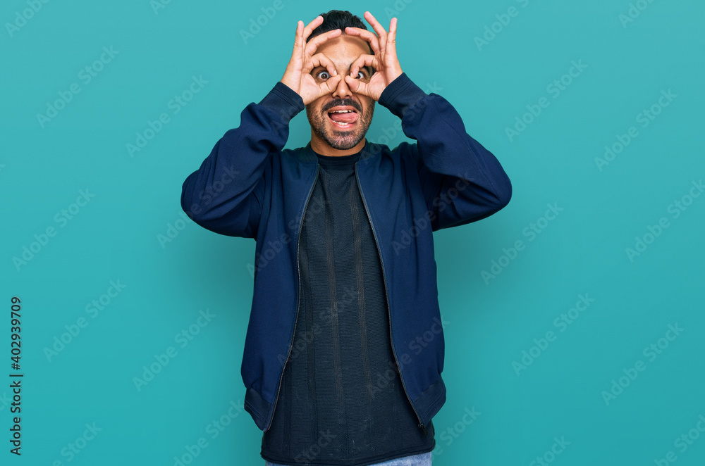 Young hispanic man wearing casual clothes doing ok gesture like binoculars sticking tongue out, eyes looking through fingers. crazy expression.