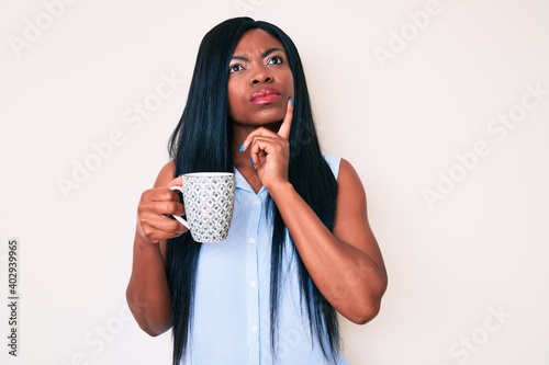 Young african american woman holding coffee serious face thinking about question with hand on chin, thoughtful about confusing idea