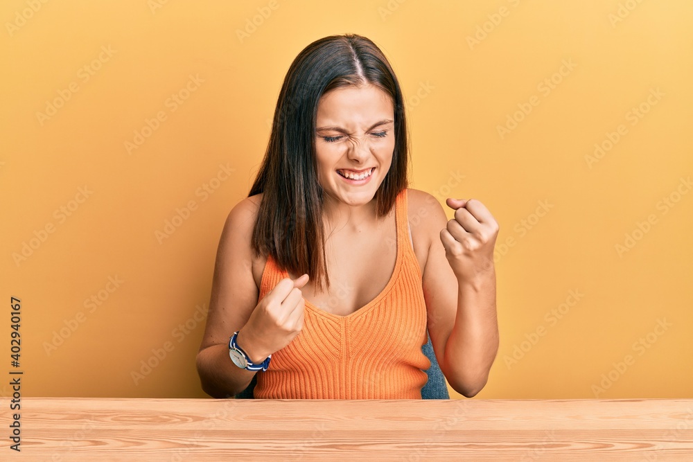 Young caucasian woman wearing casual clothes sitting on the table celebrating surprised and amazed for success with arms raised and eyes closed. winner concept. Young caucasian woman wearing casual clothes sitting on the table celebrating surprised and amazed for success with arms raised and eyes closed. winner concept.