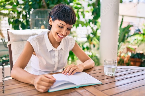 Beautiful woman with short hair sitting at the terrace on a sunny day reading a book