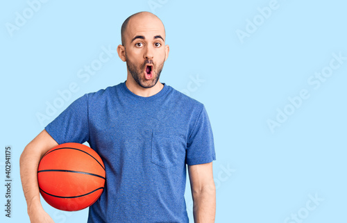 Young handsome man holding basketball ball scared and amazed with open mouth for surprise, disbelief face