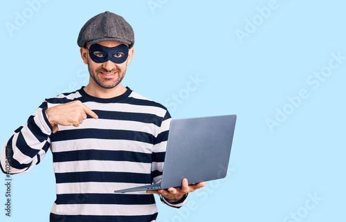 Young handsome man wearing burglar mask using laptop pointing finger to one self smiling happy and proud © Krakenimages.com
