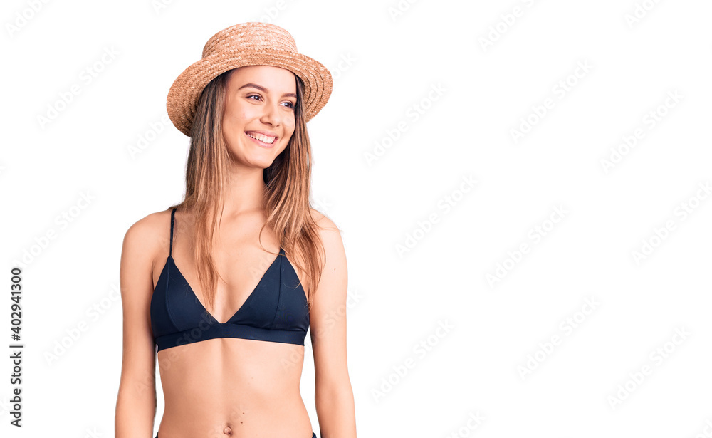 Young beautiful girl wearing bikini and hat looking away to side with smile on face, natural expression. laughing confident. Young beautiful girl wearing bikini and hat looking away to side with smile on face, natural expression. laughing confident.