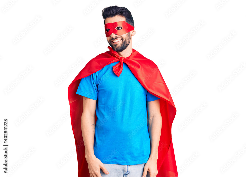 Young handsome man with beard wearing super hero costume looking away to side with smile on face, natural expression. laughing confident. Young handsome man with beard wearing super hero costume looking away to side with smile on face, natural expression. laughing confident.