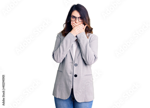 Beautiful young brunette woman wearing business clothes and glasses shocked covering mouth with hands for mistake. secret concept.