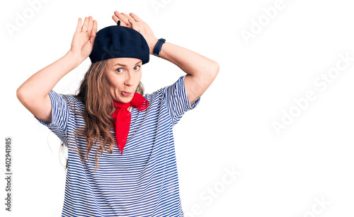 Young beautiful blonde woman wearing french beret and striped t-shirt doing bunny ears gesture with hands palms looking cynical and skeptical. easter rabbit concept. photo
