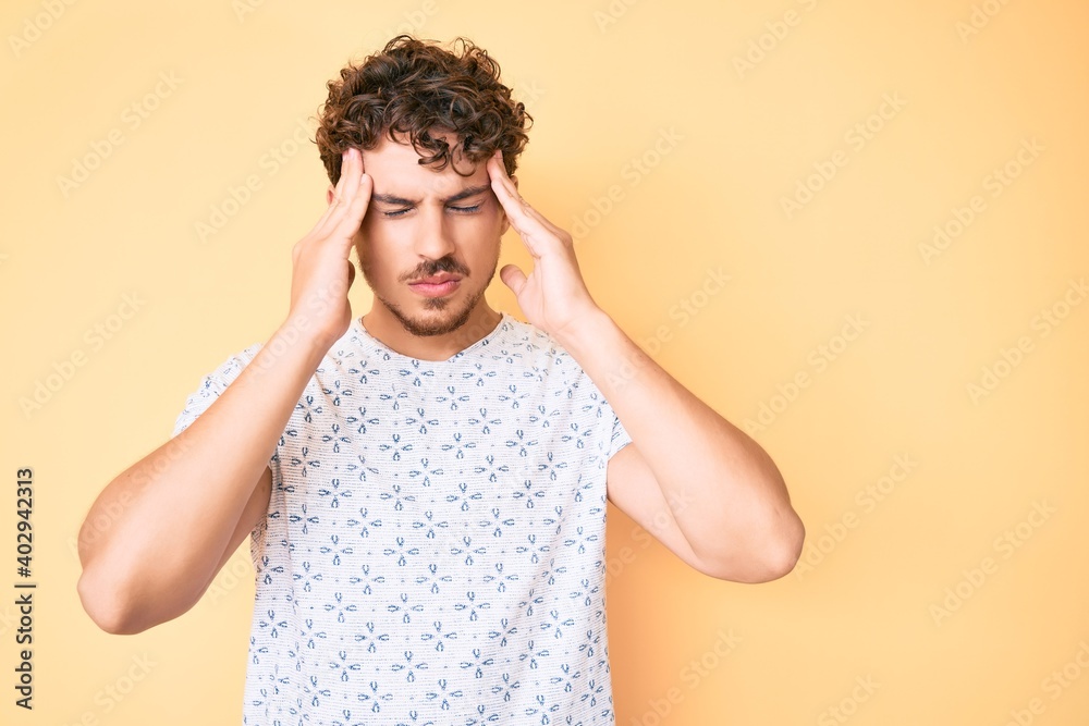 Young caucasian man with curly hair wearing casual clothes suffering from headache desperate and stressed because pain and migraine. hands on head. Young caucasian man with curly hair wearing casual clothes suffering from headache desperate and stressed because pain and migraine. hands on head.