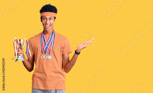 Young african american man holding champion trophy wearing medals celebrating victory with happy smile and winner expression with raised hands