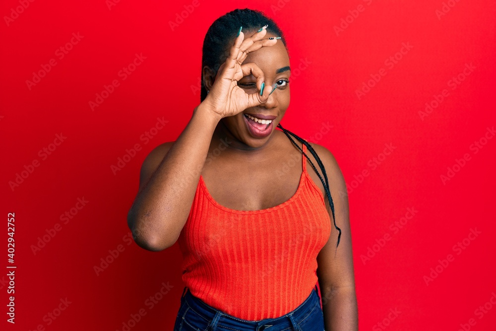 Young african american woman doing ok sign on eye winking looking at the camera with sexy expression, cheerful and happy face. Young african american woman doing ok sign on eye winking looking at the camera with sexy expression, cheerful and happy face.