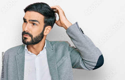 Young hispanic man wearing business clothes confuse and wondering about question. uncertain with doubt, thinking with hand on head. pensive concept.