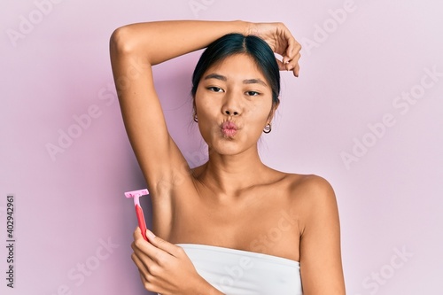 Young chinese woman wearing shower towel using razor looking at the camera blowing a kiss being lovely and sexy. love expression. photo