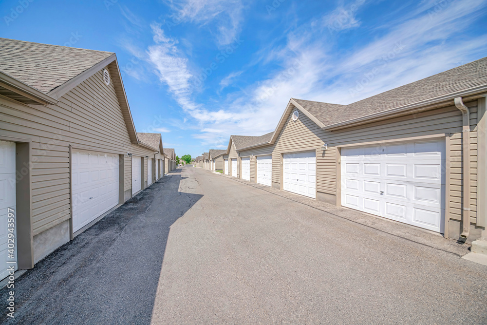 Exterior of houses on a sunny day with white garage doors along paved road Exterior of houses on a sunny day with white garage doors along paved road