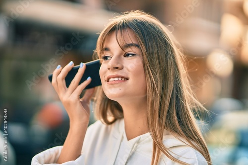 Caucasian sporty teenager girl listening audio message using smartphone at the city.