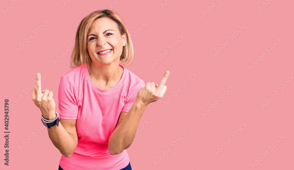 Young blonde woman wearing sportswear showing middle finger doing fuck you bad expression, provocation and rude attitude. screaming excited Young blonde woman wearing sportswear showing middle finger doing fuck you bad expression, provocation and rude attitude. screaming excited