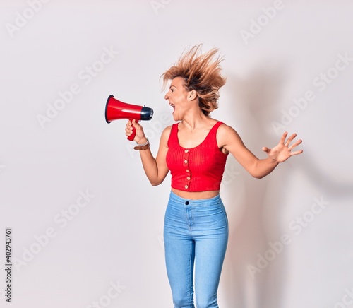 Young beautiful caucasian woman screaming using megaphone. Jumping over isolated white background
