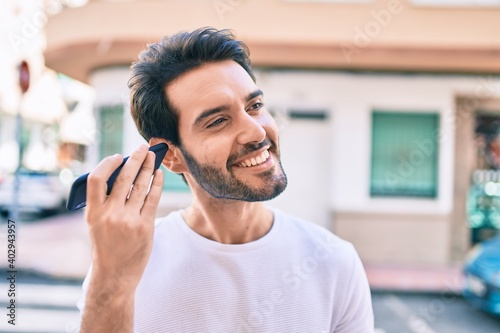 Young hispanic man smiling happy listening audio message using smartphone at city.