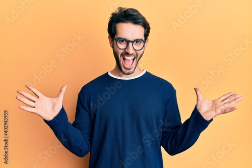 Young hispanic man wearing casual clothes and glasses celebrating victory with happy smile and winner expression with raised hands