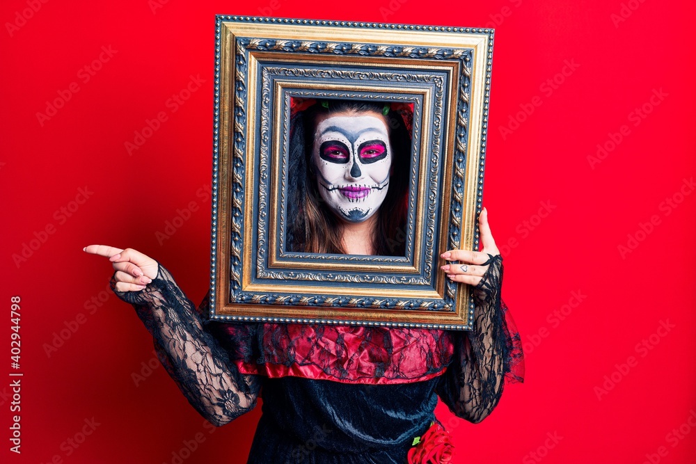 Obraz premium Young woman wearing day of the dead costume holding empty frame smiling happy pointing with hand and finger to the side