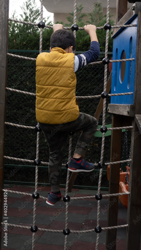A wearing mask kid climbing on net obstacle in the outoor park