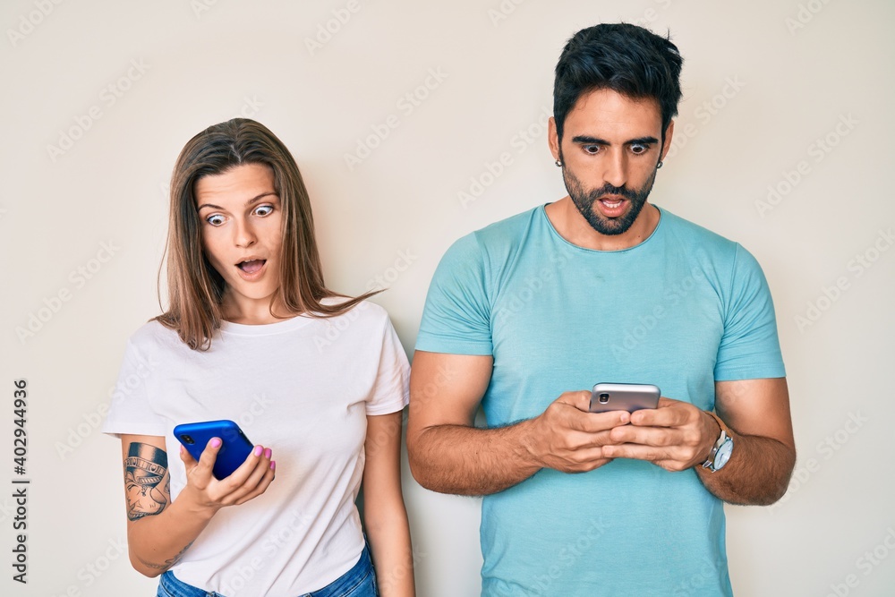 Beautiful young couple of boyfriend and girlfriend using smartphone scared and amazed with open mouth for surprise, disbelief face Beautiful young couple of boyfriend and girlfriend using smartphone scared and amazed with open mouth for surprise, disbelief face