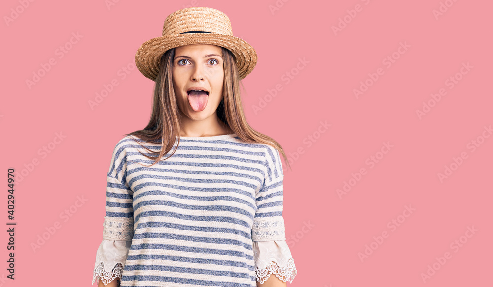 Beautiful caucasian woman wearing summer hat sticking tongue out happy with funny expression. emotion concept. Beautiful caucasian woman wearing summer hat sticking tongue out happy with funny expression. emotion concept.