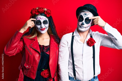 Couple wearing day of the dead costume over red pointing unhappy to pimple on forehead  ugly infection of blackhead. acne and skin problem