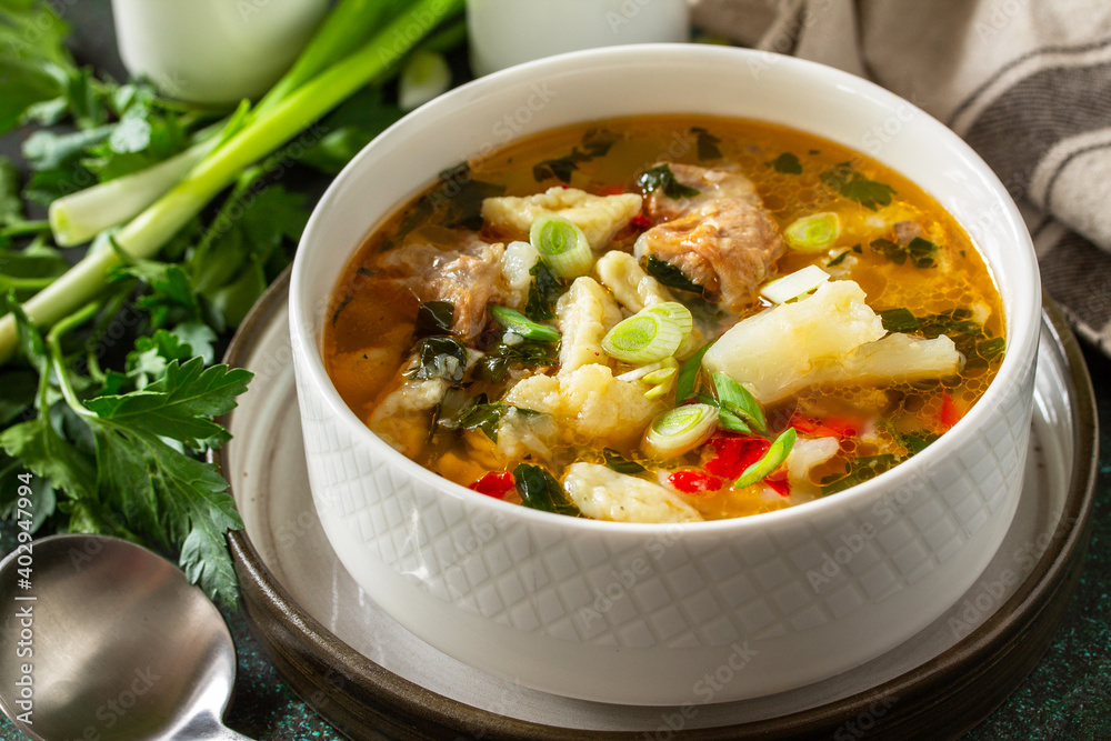 Hot delicious beef soup close-up. Homemade soup with meat, vegetables and gnocchi on a dark stone background. Hot delicious beef soup close-up. Homemade soup with meat, vegetables and gnocchi on a dark stone background.