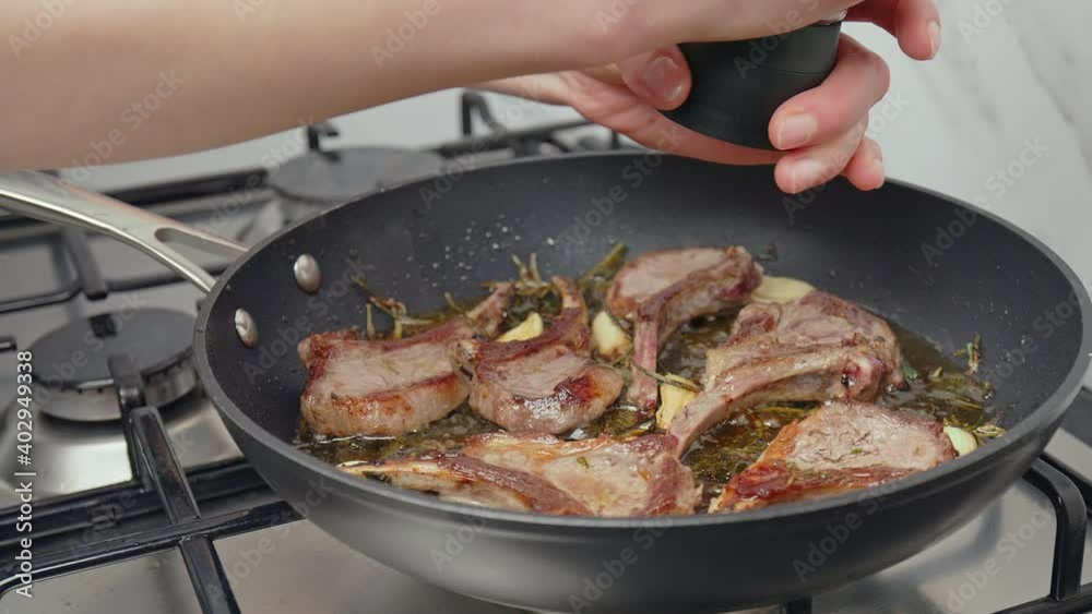Close-up seasoning with salt and pepper raw lamb ribs cutlets in a frying pan. Concept of cooking healthy food, lamb meat with rosemary, sage, garlic, olive oil spices in 4k in slow-motion. Close-up seasoning with salt and pepper raw lamb ribs cutlets in a frying pan. Concept of cooking healthy food, lamb meat with rosemary, sage, garlic, olive oil spices in 4k in slow-motion.