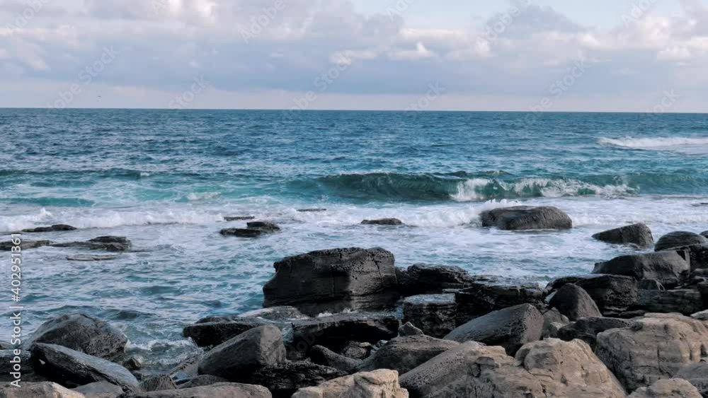 Sea waves splashing on rocky shore with blue sea background. Rocky shoreline with waves swept in stormy day. Sea wave breaks on stones with foam. Sea waves splashing on rocky shore with blue sea background. Rocky shoreline with waves swept in stormy day. Sea wave breaks on stones with foam.